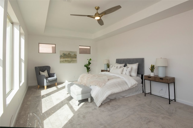 bedroom with a raised ceiling, light colored carpet, and ceiling fan