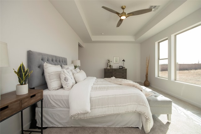 carpeted bedroom featuring a raised ceiling and ceiling fan