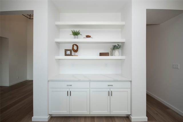 bar featuring dark wood-type flooring, white cabinetry, and light stone counters