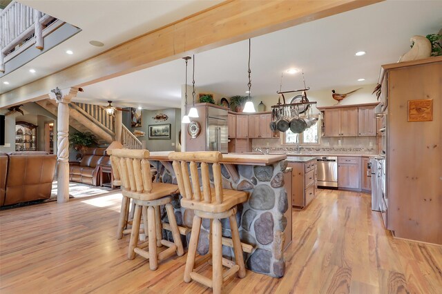 kitchen with an island with sink, backsplash, decorative light fixtures, high quality appliances, and light wood-type flooring