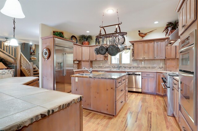 kitchen featuring appliances with stainless steel finishes, backsplash, sink, light hardwood / wood-style flooring, and a kitchen island with sink