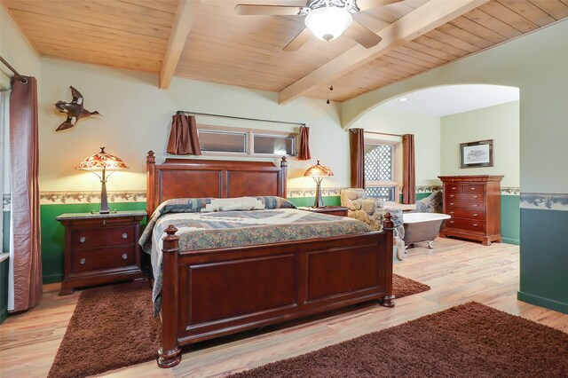 bedroom with beamed ceiling, a stone fireplace, light wood-type flooring, ceiling fan, and wood ceiling