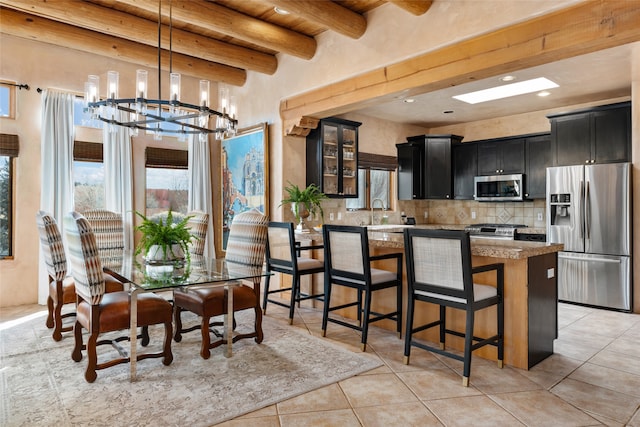 dining area featuring light tile patterned flooring, sink, a chandelier, and beam ceiling