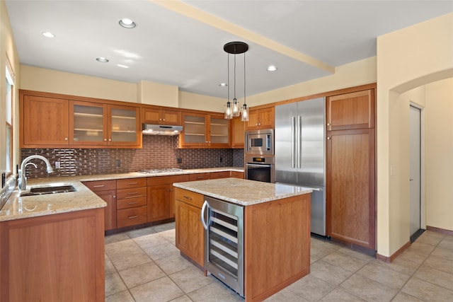 kitchen with wine cooler, built in appliances, hanging light fixtures, a kitchen island, and light stone countertops