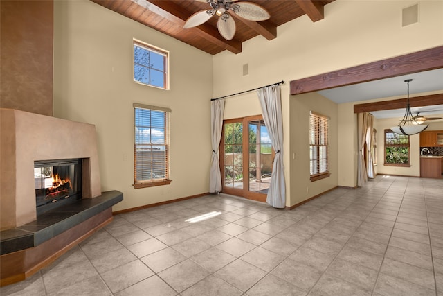 unfurnished living room featuring a wealth of natural light, a tiled fireplace, ceiling fan, and wooden ceiling