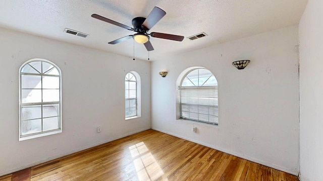 unfurnished room featuring plenty of natural light, light hardwood / wood-style flooring, ceiling fan, and a textured ceiling