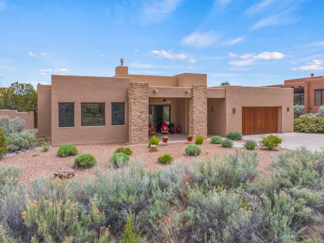 adobe home with driveway, a garage, stone siding, and stucco siding