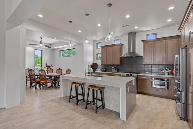 kitchen with a center island with sink, visible vents, a sink, appliances with stainless steel finishes, and wall chimney exhaust hood