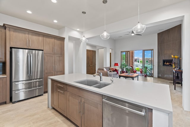 kitchen with a sink, open floor plan, stainless steel appliances, a large fireplace, and light countertops