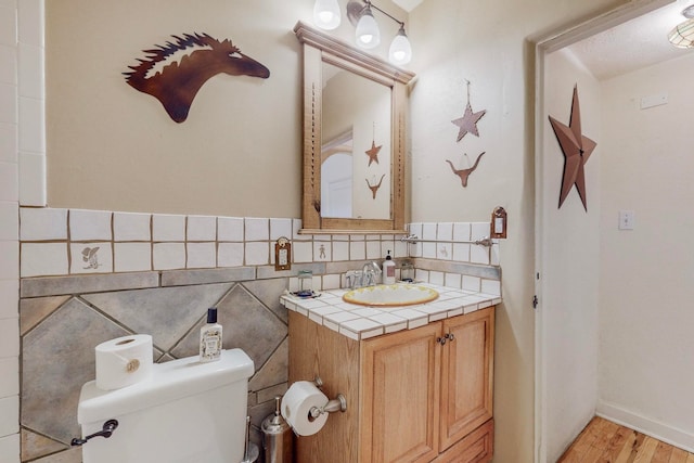 bathroom with tile walls, backsplash, hardwood / wood-style flooring, toilet, and vanity