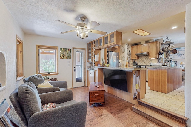 living room with a textured ceiling, light wood-type flooring, and ceiling fan