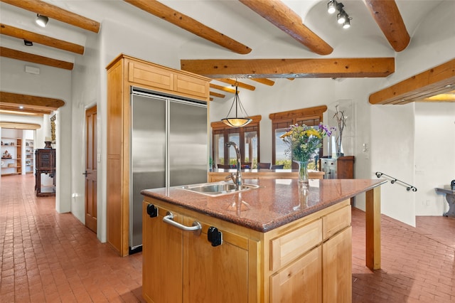 kitchen with beamed ceiling, an island with sink, sink, built in fridge, and light brown cabinetry