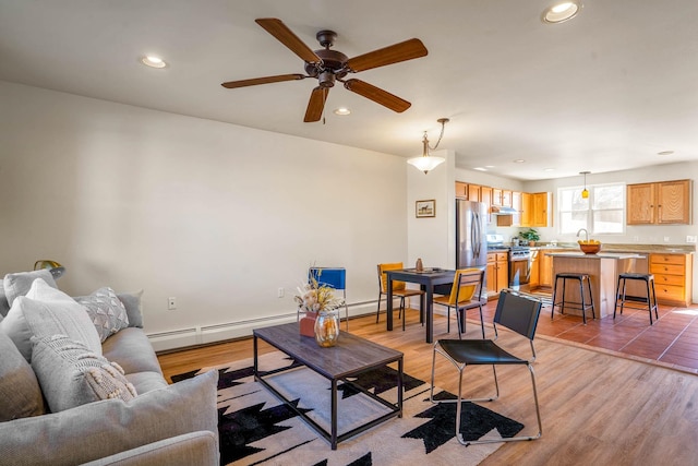 living room featuring light wood-type flooring, recessed lighting, baseboards, baseboard heating, and ceiling fan