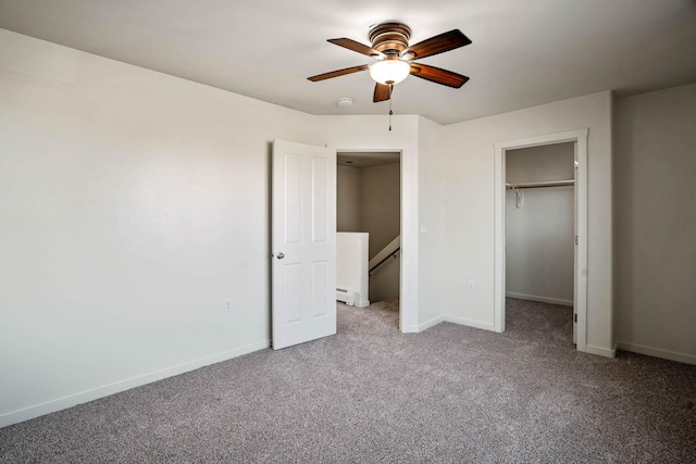 unfurnished bedroom featuring a ceiling fan, baseboards, a spacious closet, a baseboard heating unit, and carpet flooring