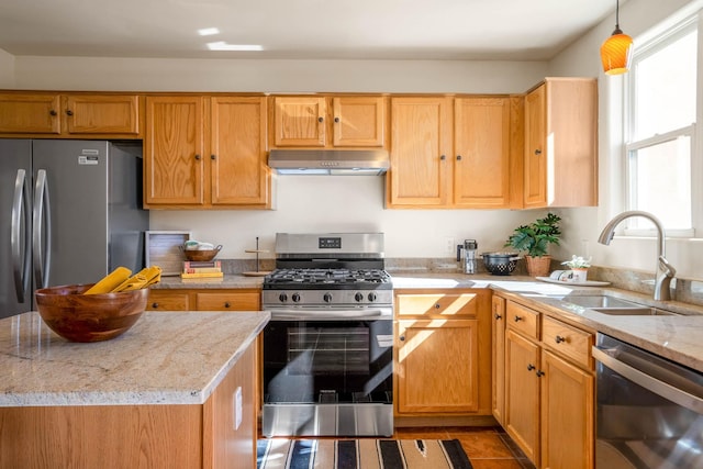 kitchen featuring under cabinet range hood, decorative light fixtures, light stone counters, a sink, and appliances with stainless steel finishes