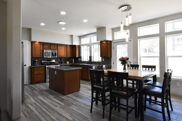 kitchen featuring stainless steel appliances, pendant lighting, dark wood-type flooring, backsplash, and a kitchen island