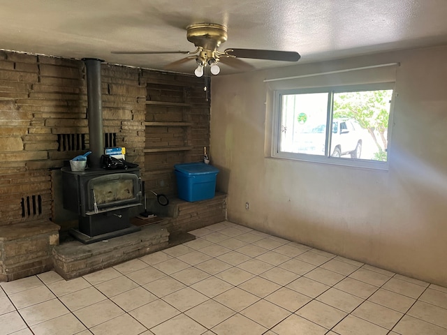 unfurnished living room with ceiling fan, a textured ceiling, a wood stove, and light tile floors