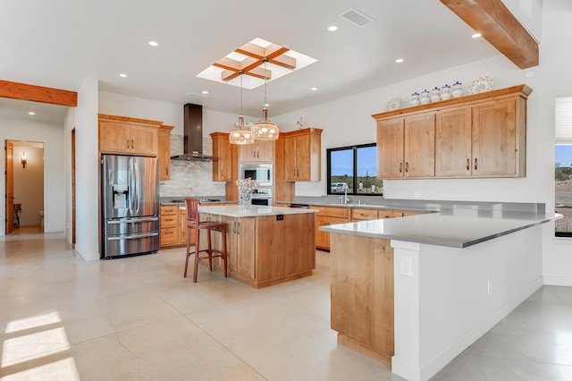 kitchen featuring wall chimney range hood, a skylight, appliances with stainless steel finishes, a kitchen island, and a breakfast bar area