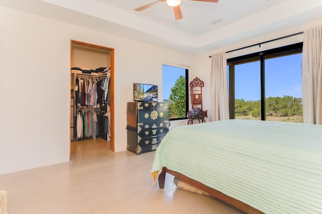 bedroom featuring a raised ceiling, a walk in closet, ceiling fan, and a closet