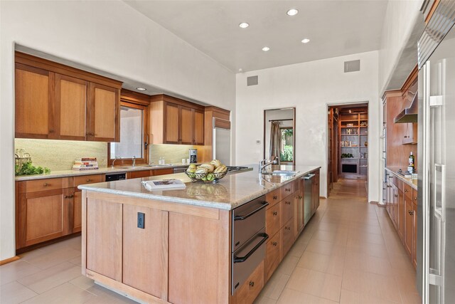 kitchen with an island with sink, sink, backsplash, light stone counters, and plenty of natural light