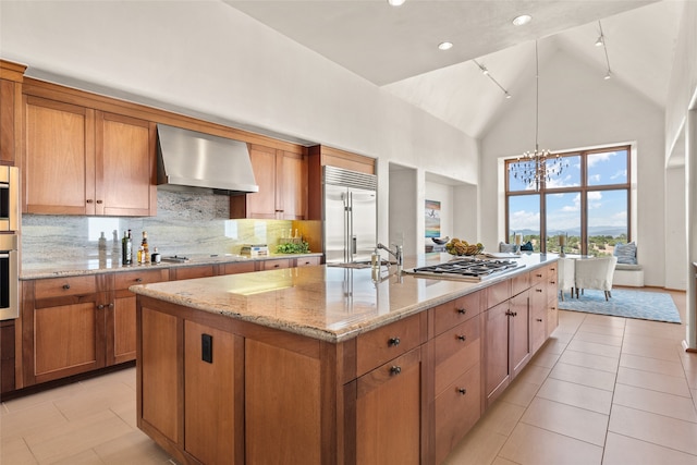 kitchen with appliances with stainless steel finishes, high vaulted ceiling, light stone counters, a center island with sink, and wall chimney exhaust hood