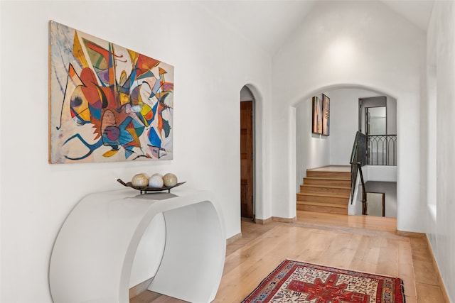 hallway with high vaulted ceiling and light hardwood / wood-style floors