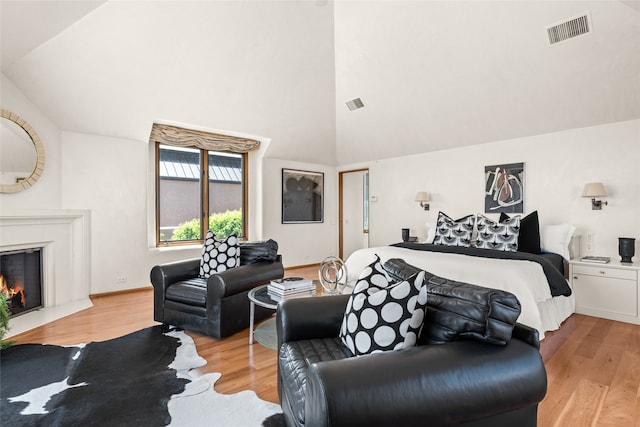 bedroom featuring high vaulted ceiling, light wood-type flooring, and a high end fireplace