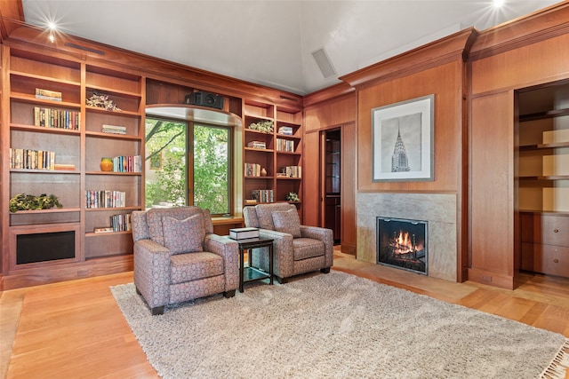 living area with a premium fireplace, vaulted ceiling, hardwood / wood-style floors, and built in shelves