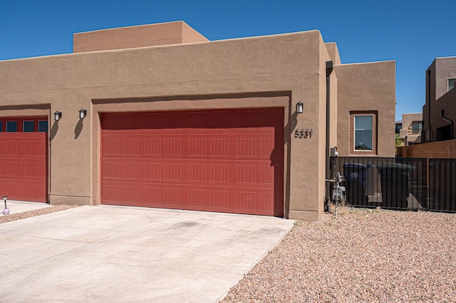pueblo-style house with concrete driveway, stucco siding, and central AC