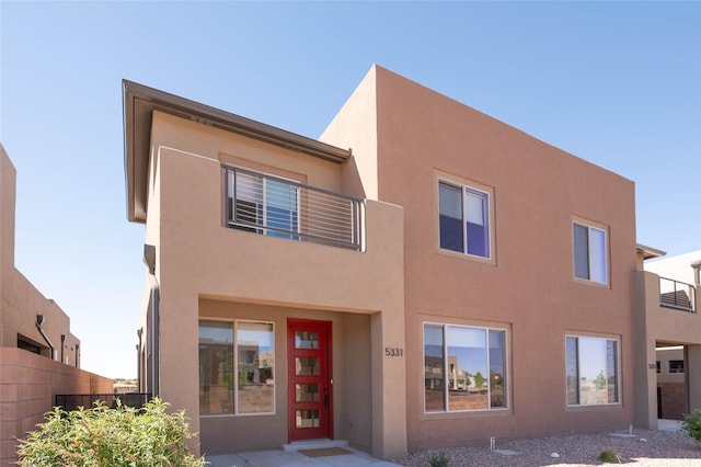 view of front facade featuring stucco siding, fence, and a balcony