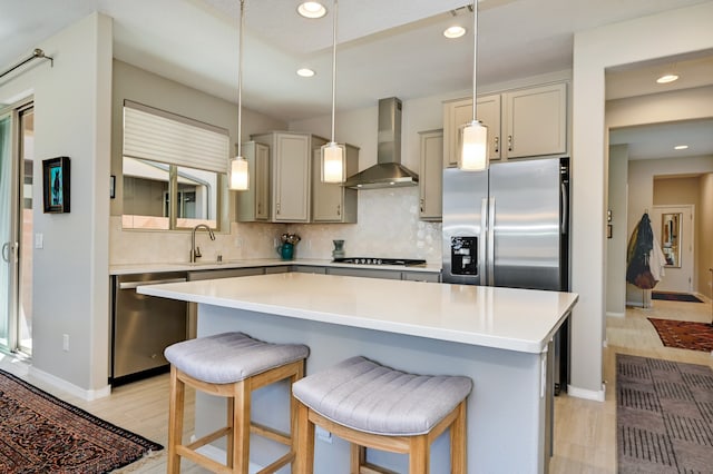 kitchen featuring light wood-type flooring, a kitchen bar, stainless steel appliances, a center island, and wall chimney range hood