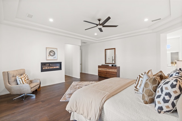 bedroom featuring visible vents, dark wood finished floors, recessed lighting, a glass covered fireplace, and a raised ceiling