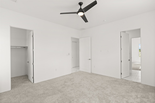 unfurnished bedroom with ceiling fan, a walk in closet, a closet, and light colored carpet