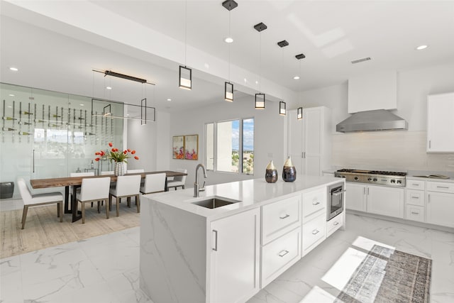 kitchen featuring marble finish floor, a kitchen island with sink, a sink, recessed lighting, and wall chimney range hood