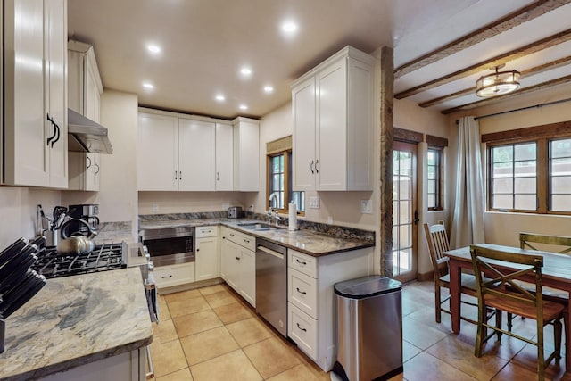 kitchen with dark stone counters, white cabinets, sink, appliances with stainless steel finishes, and beam ceiling