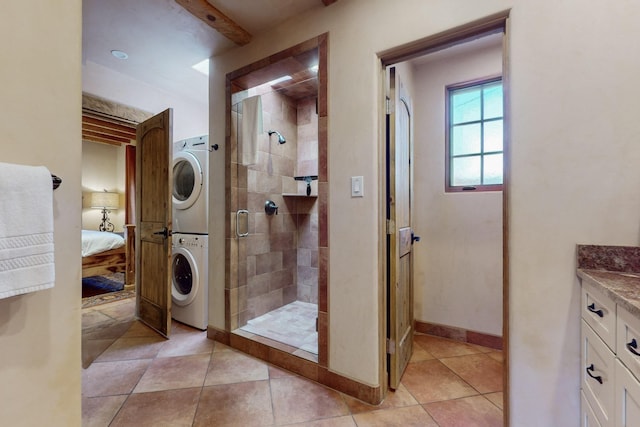 bathroom with a shower with door, vanity, stacked washing maching and dryer, and tile patterned flooring