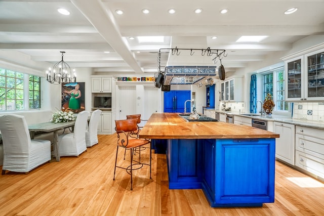 kitchen with light hardwood / wood-style flooring, a center island with sink, wooden counters, backsplash, and white cabinets