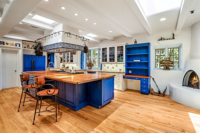 kitchen with beamed ceiling, butcher block countertops, a breakfast bar, and light hardwood / wood-style flooring