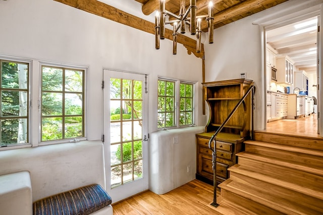 entryway featuring beam ceiling, light hardwood / wood-style flooring, and an inviting chandelier