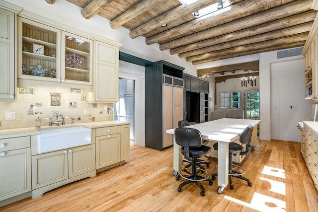 kitchen featuring light hardwood / wood-style flooring, cream cabinets, tasteful backsplash, beam ceiling, and sink