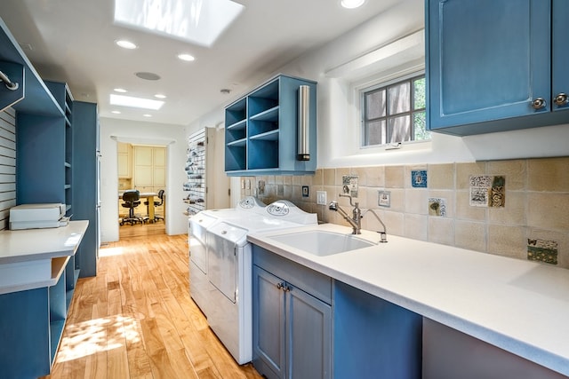 laundry room with sink, light hardwood / wood-style flooring, washing machine and clothes dryer, and cabinets