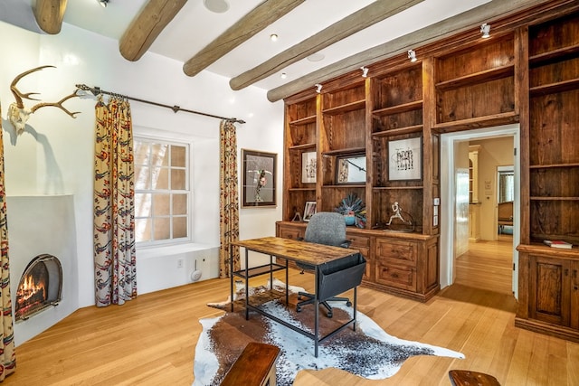 office featuring a wealth of natural light, beamed ceiling, light hardwood / wood-style flooring, and a fireplace