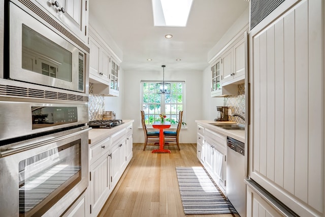 kitchen with decorative light fixtures, backsplash, light wood-type flooring, appliances with stainless steel finishes, and sink