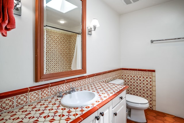 bathroom featuring tile floors, a skylight, oversized vanity, and toilet