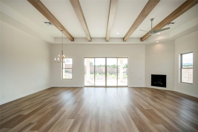 unfurnished living room with beamed ceiling, ceiling fan with notable chandelier, a large fireplace, and wood-type flooring