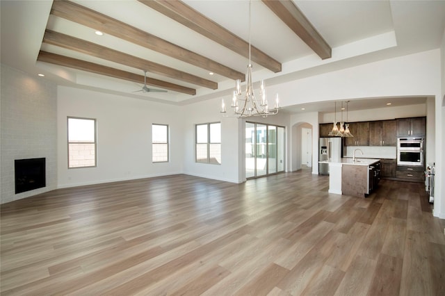 unfurnished living room featuring hardwood / wood-style flooring, ceiling fan with notable chandelier, beam ceiling, and a fireplace