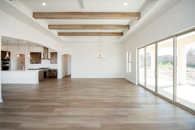 unfurnished living room with wood-type flooring, sink, a notable chandelier, and beam ceiling