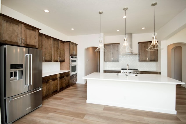 kitchen with a center island with sink, wall chimney exhaust hood, light hardwood / wood-style floors, and appliances with stainless steel finishes