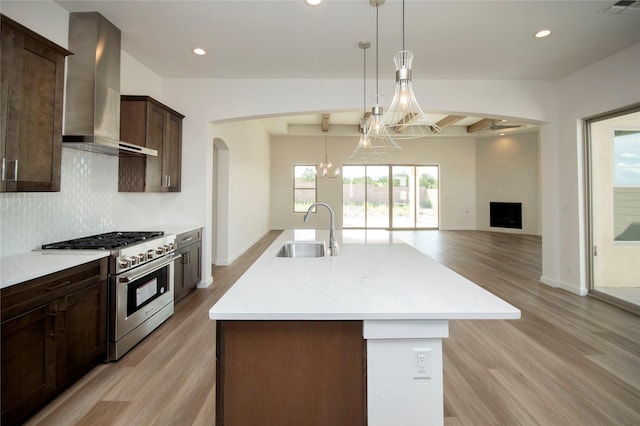 kitchen with stainless steel range, wall chimney exhaust hood, sink, light stone counters, and light hardwood / wood-style floors