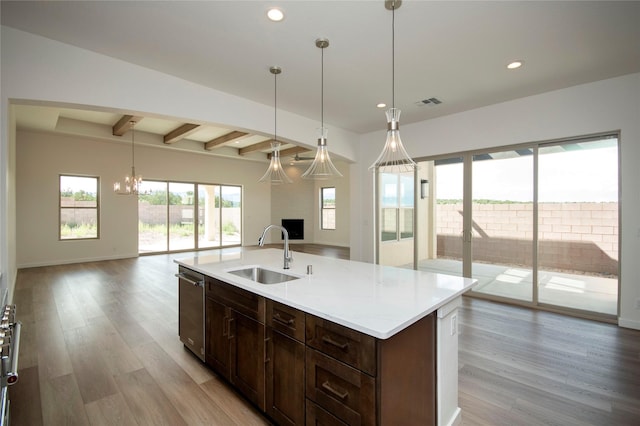 kitchen featuring sink, pendant lighting, beamed ceiling, light hardwood / wood-style floors, and an island with sink